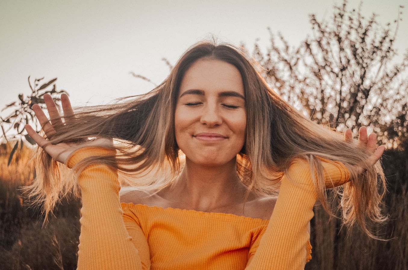 a woman in a yellow shirt is holding her hair in a field .