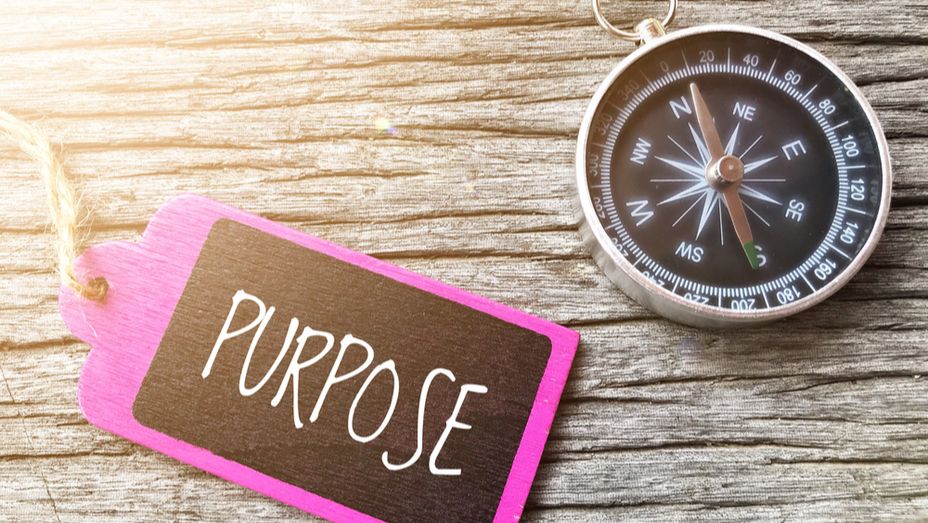 a compass is sitting on a wooden table next to a pink tag that says `` purpose '' .