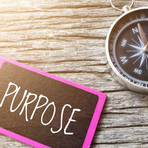 a compass is sitting on a wooden table next to a pink tag that says `` purpose '' .