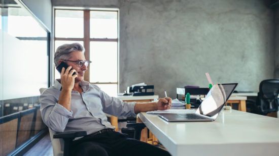 a man is sitting at a desk talking on a cell phone .