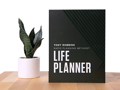 a life planner is sitting on a wooden table next to a potted plant .