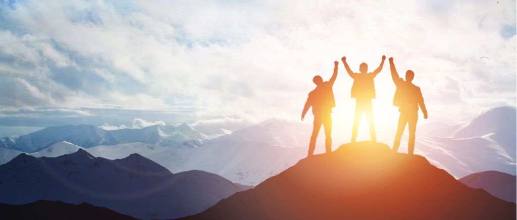a group of people are standing on top of a mountain with their arms in the air .