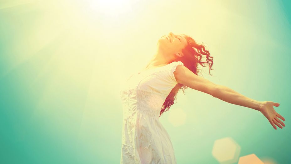 a woman in a white dress is standing with her arms outstretched in front of the sun .