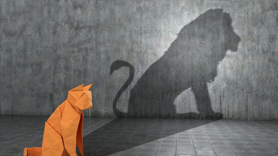 an origami cat is sitting in front of a wall with a shadow of a lion on it .