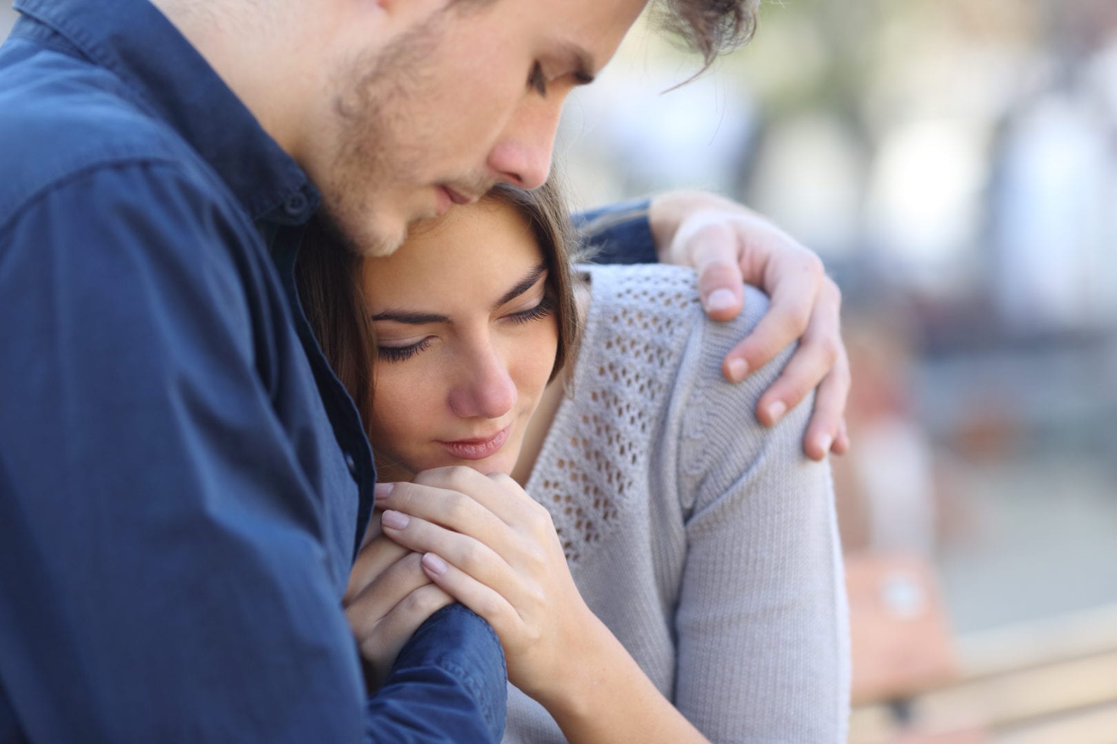 a man is comforting a woman who is sitting on a bench .