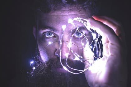 a man with a beard is holding a string of lights in front of his face .