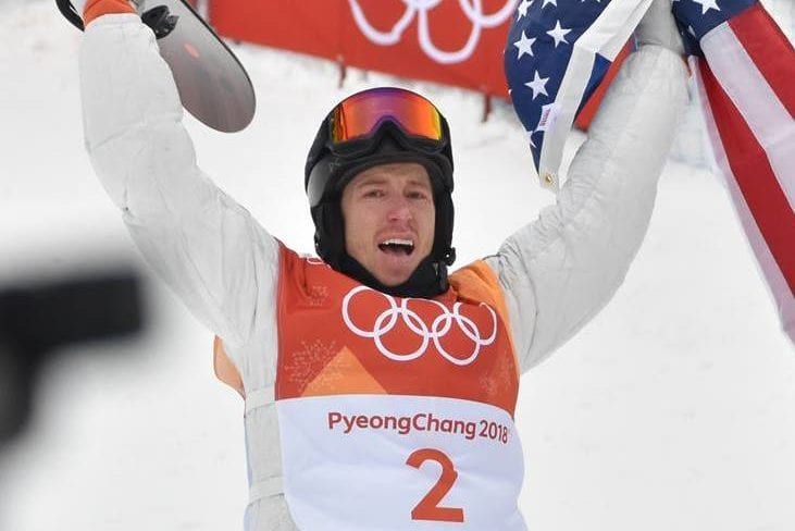 a man is holding a snowboard and an american flag in the air .