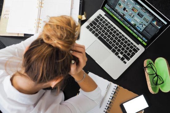 a woman is sitting at a desk with her head in her hands in front of a laptop computer .