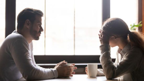 a man and a woman are sitting at a table talking to each other .