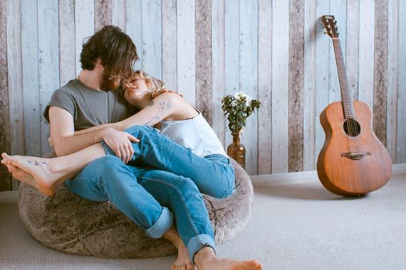 a man and a woman are sitting on a bean bag chair next to a guitar .