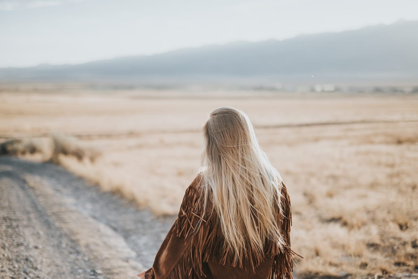 a woman is sitting on the side of a dirt road in the middle of a field .