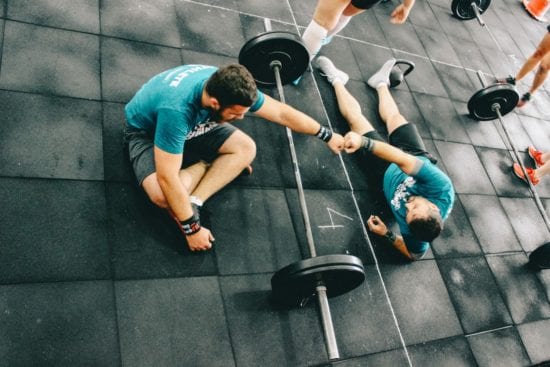 a man is helping another man lift a barbell in a gym .