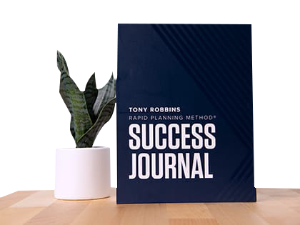 a book titled success journal is sitting on a wooden table next to a potted plant .