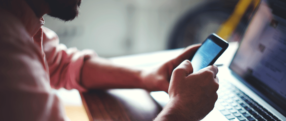 a man is using a cell phone in front of a laptop
