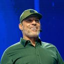 a man in a green shirt and hat is standing on a stage giving a speech .