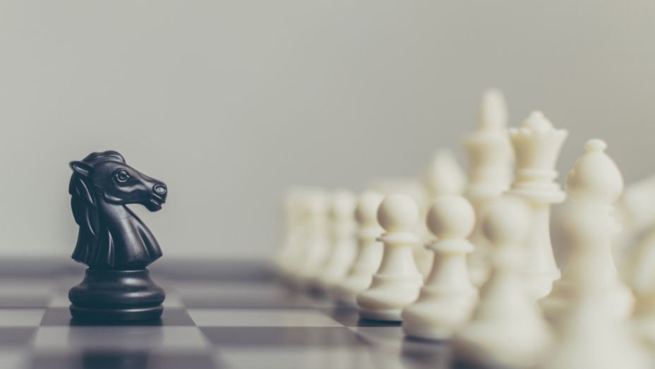a black knight is standing in front of a row of white chess pieces on a chess board .