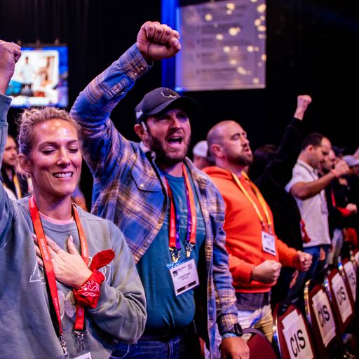 a group of people are standing in a room with their hands in the air .