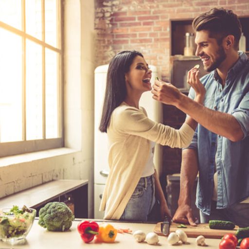 a man is feeding a woman a piece of food in the kitchen .