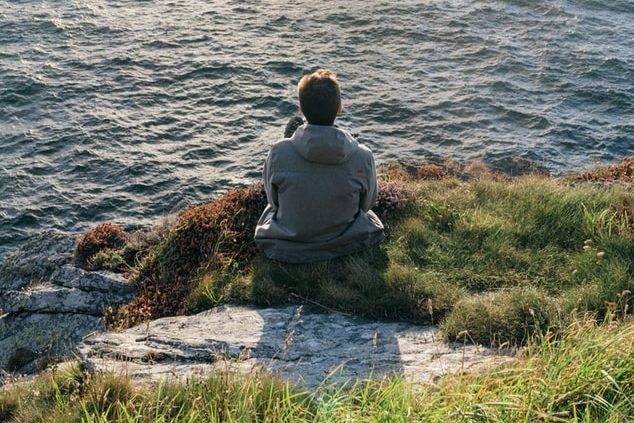 a man is sitting on a rock overlooking the ocean .