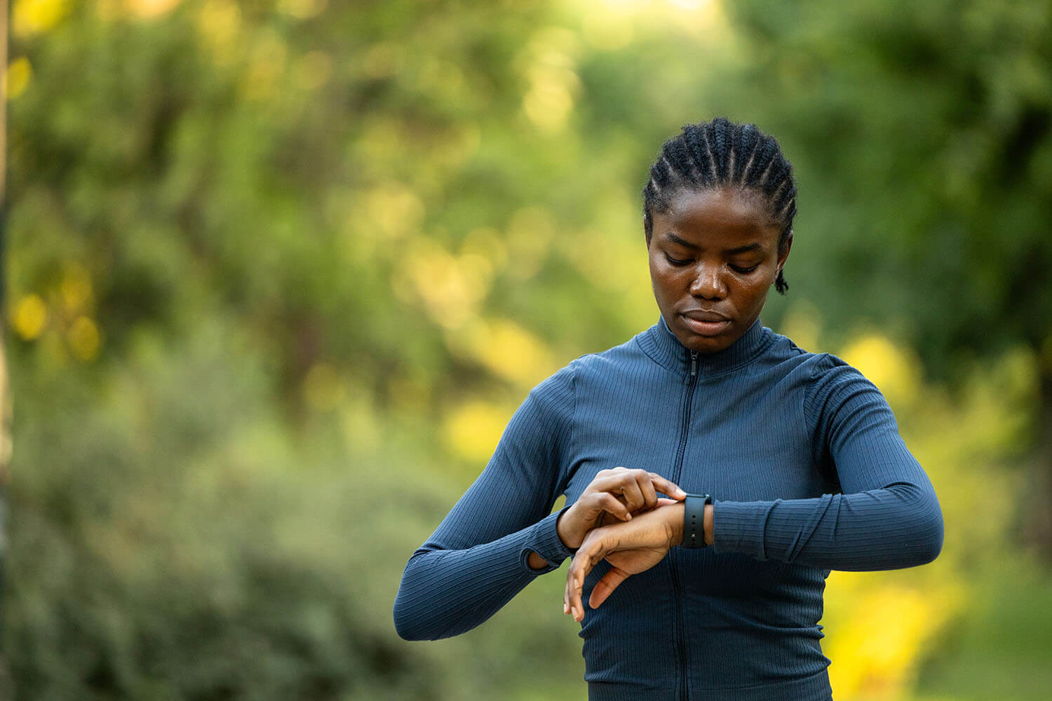 A Black woman in athletic wear looks at her smartwatch outdoors.