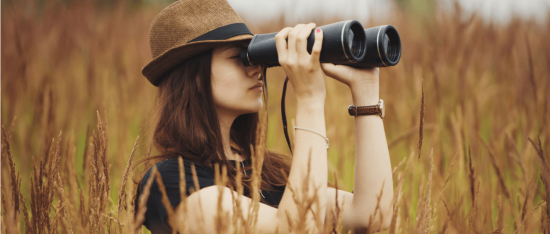 a woman in a hat looks through binoculars in a field