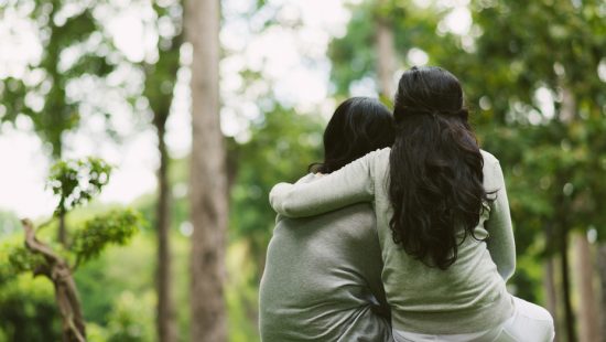 two women are hugging each other in the woods .
