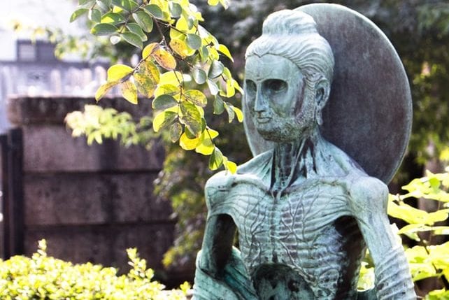 a statue of a man with a beard and a hat is sitting in front of a tree .