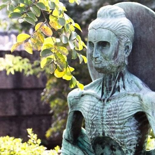 a statue of a man with a beard and a hat is sitting in front of a tree .