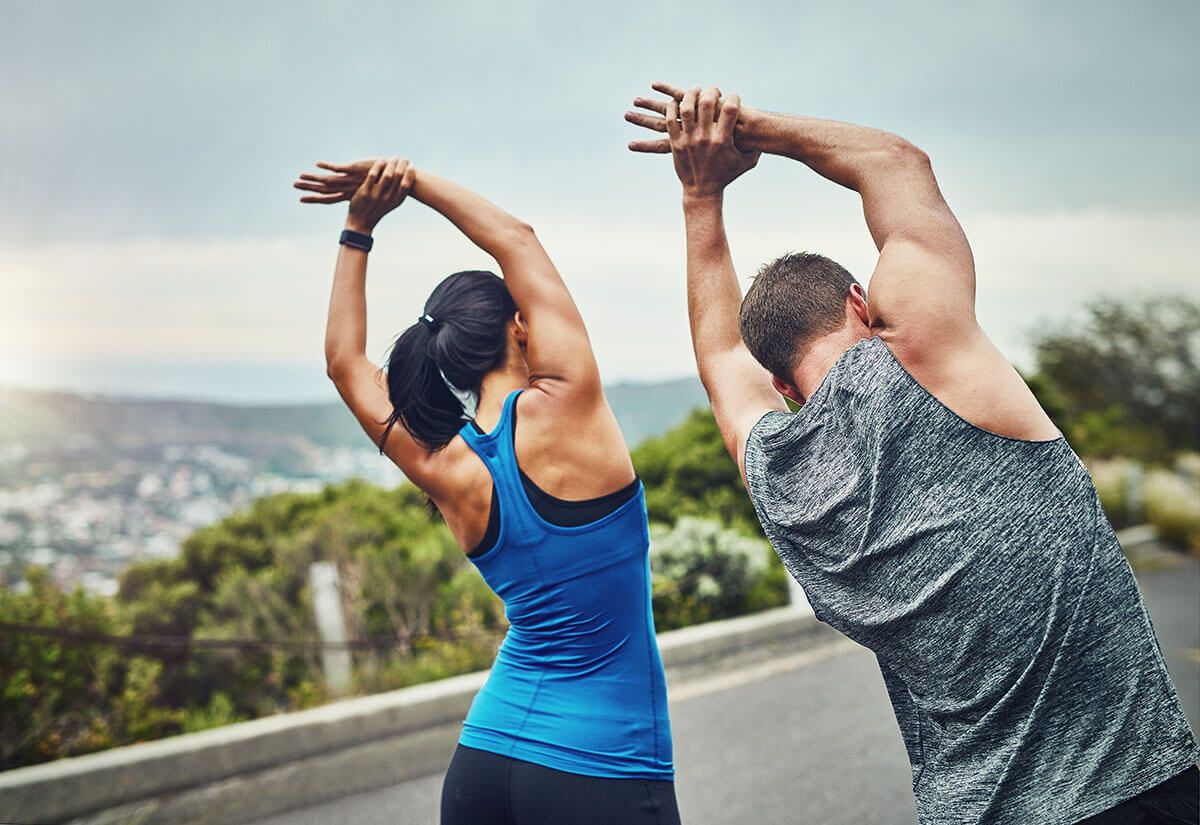 a man and a woman are stretching their arms on a road .