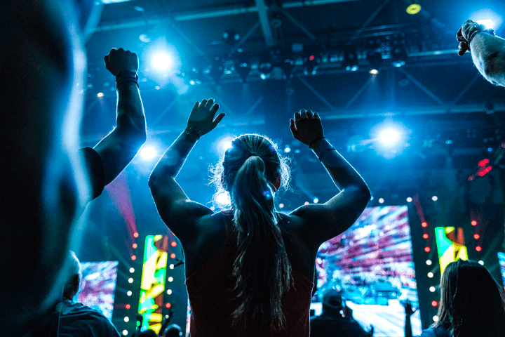 a woman stands in front of a crowd with her arms in the air
