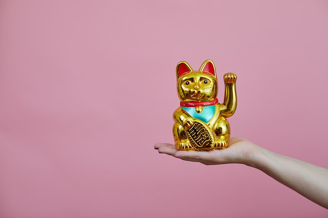 a woman 's hand is holding a golden lucky cat on a pink background .