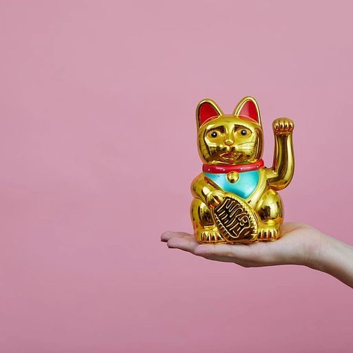 a woman 's hand is holding a golden lucky cat on a pink background .