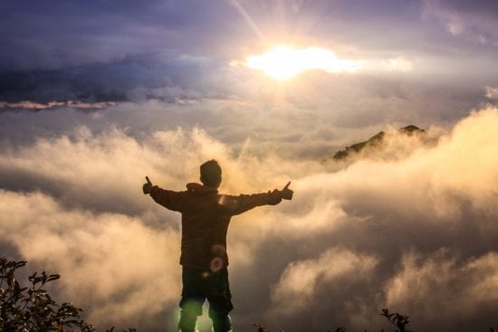 a man is standing on top of a mountain with his arms outstretched .