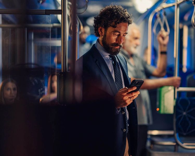 A man in a suit looks at his phone while standing on a bus or train.