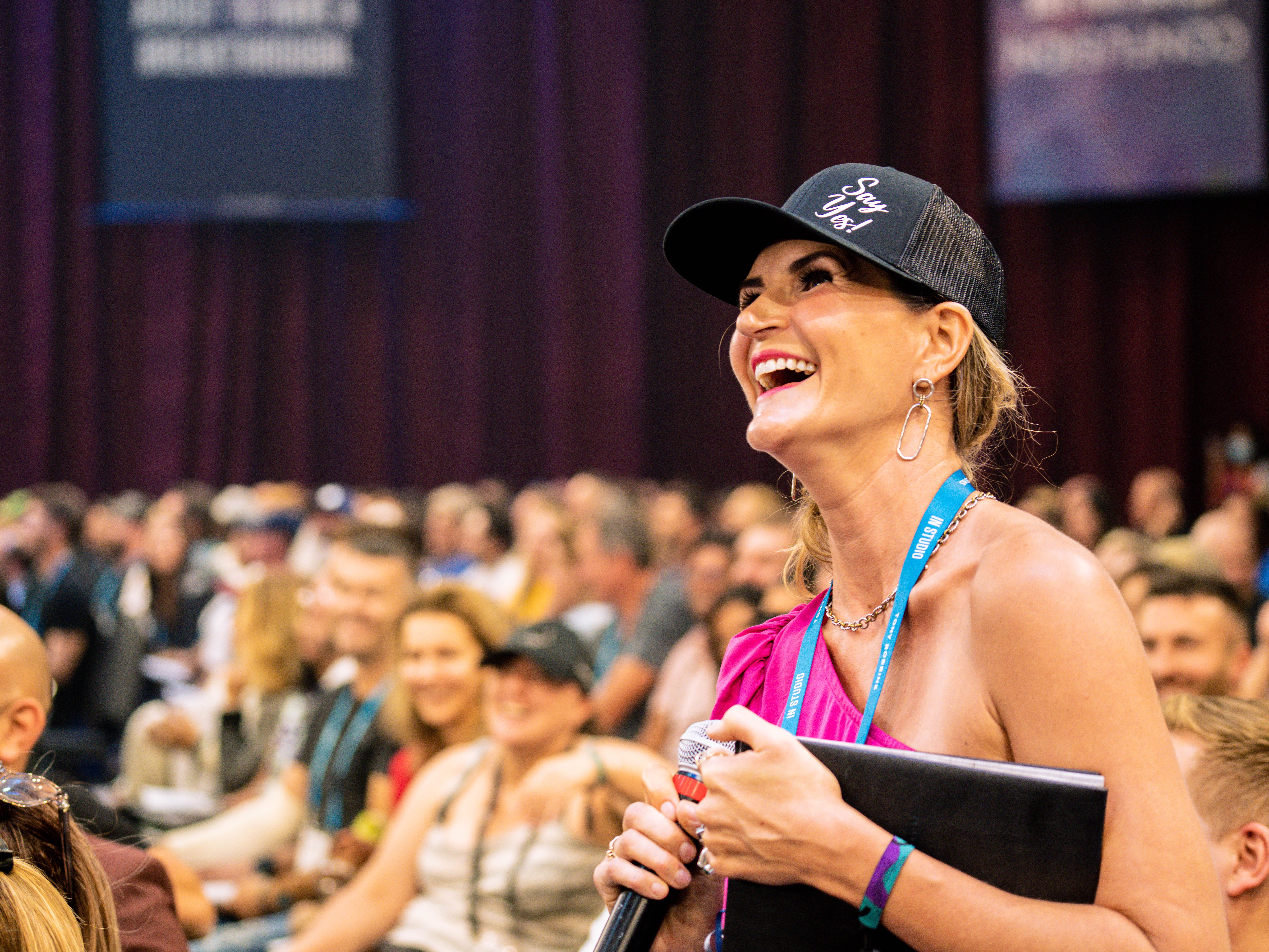 a woman is laughing while holding a microphone in front of a crowd .