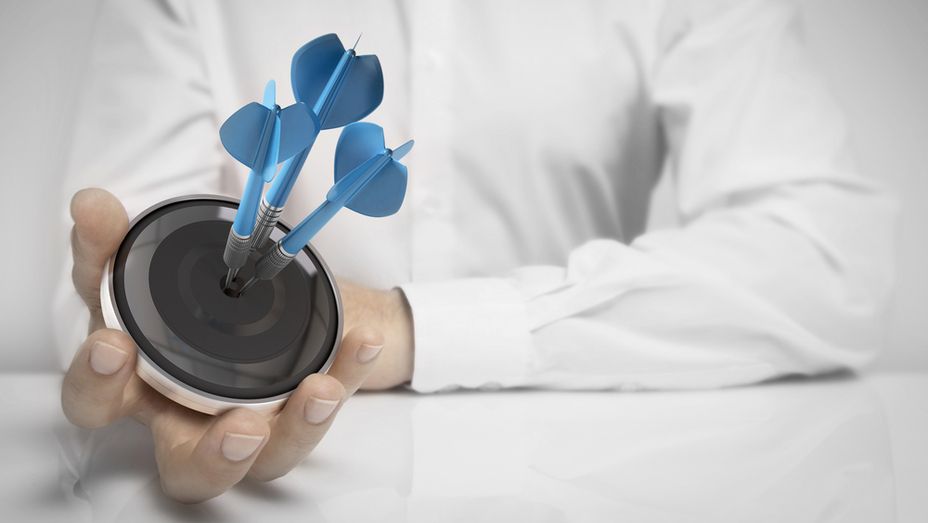 a person is holding a target with three darts in it .