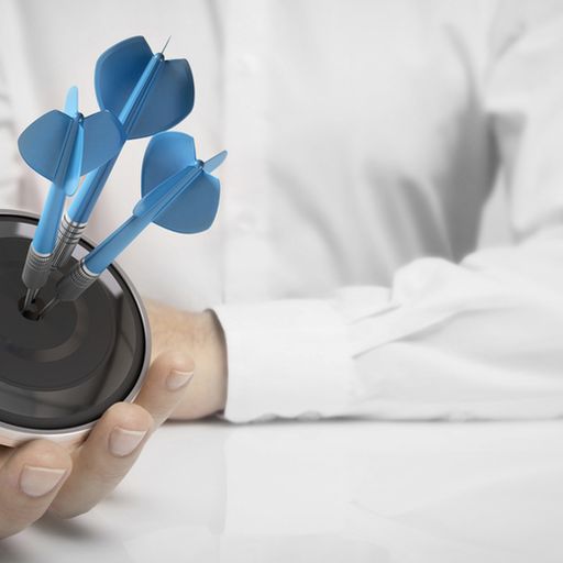 a person is holding a target with three darts in it .