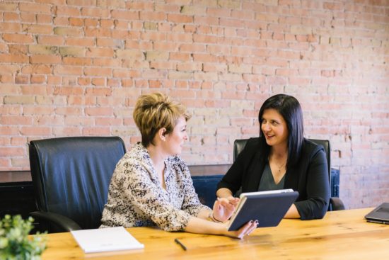 two women are sitting at a table looking at a tablet .