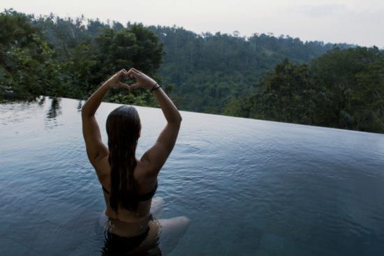 a woman is sitting in a swimming pool making a heart shape with her hands .
