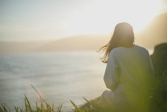 a woman is sitting on the edge of a cliff overlooking the ocean .