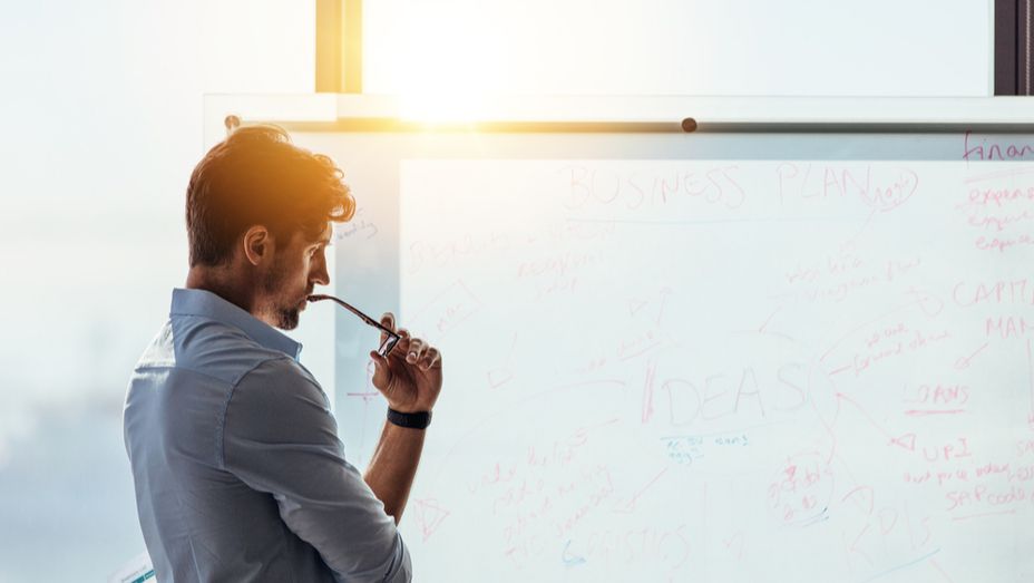 a man is standing in front of a whiteboard with a pen in his mouth .
