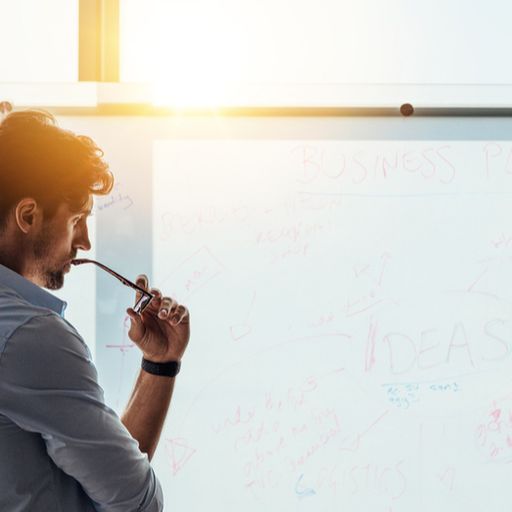 a man is standing in front of a whiteboard with a pen in his mouth .