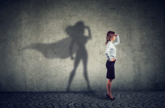 a woman is standing in front of a wall with her shadow of a superhero on it .