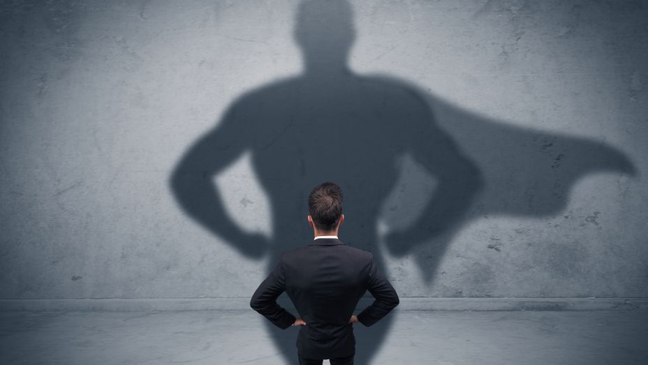 a man in a suit is standing in front of a wall with a shadow of a superhero on his back .