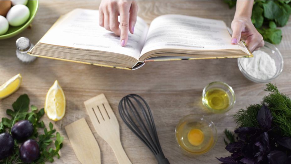 a woman is reading a cookbook on a wooden table .