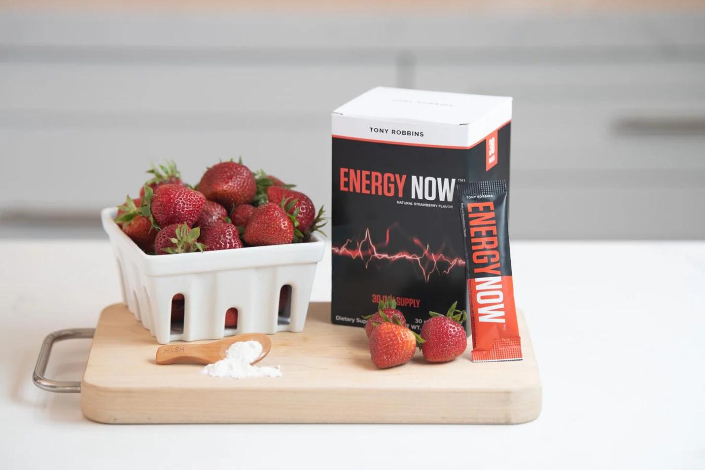 a box of energy now next to a bowl of strawberries on a cutting board .