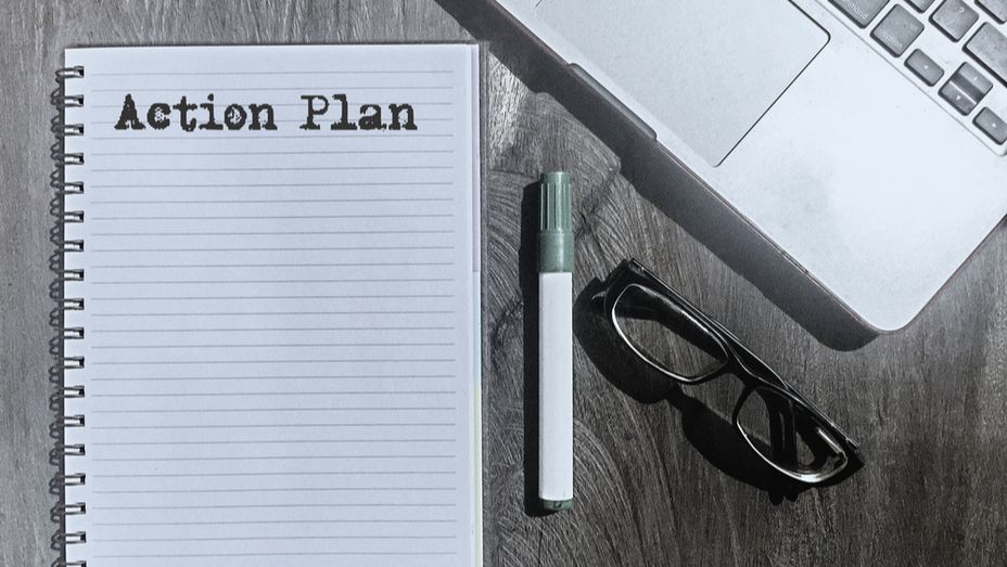 a notebook with the words action plan written on it is on a wooden table next to a laptop and glasses .