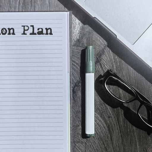 a notebook with the words action plan written on it is on a wooden table next to a laptop and glasses .