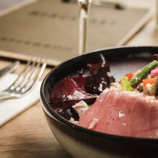 a bowl of food with meat , vegetables and a glass of wine on a table .