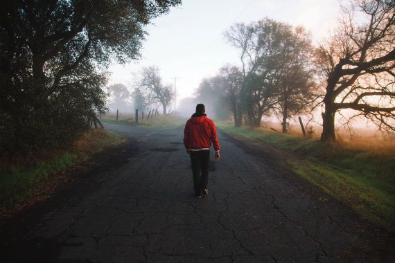 a man in a red jacket is walking down a foggy road .